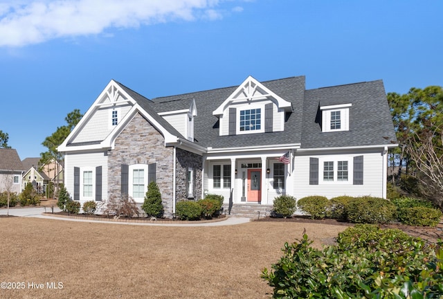 view of front of house featuring a porch, a shingled roof, stone siding, and a front yard