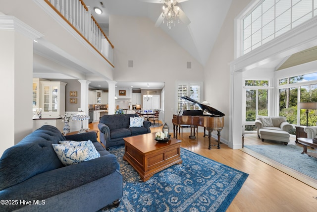 living room featuring ceiling fan with notable chandelier, ornate columns, high vaulted ceiling, and light hardwood / wood-style flooring