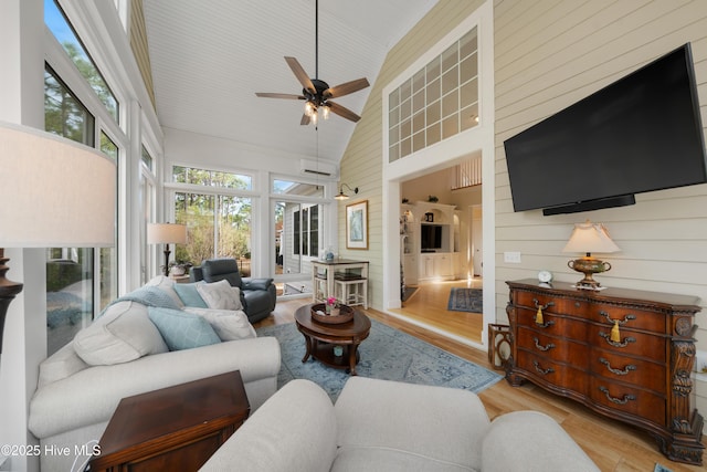 living room with ceiling fan, high vaulted ceiling, light hardwood / wood-style floors, and wood walls