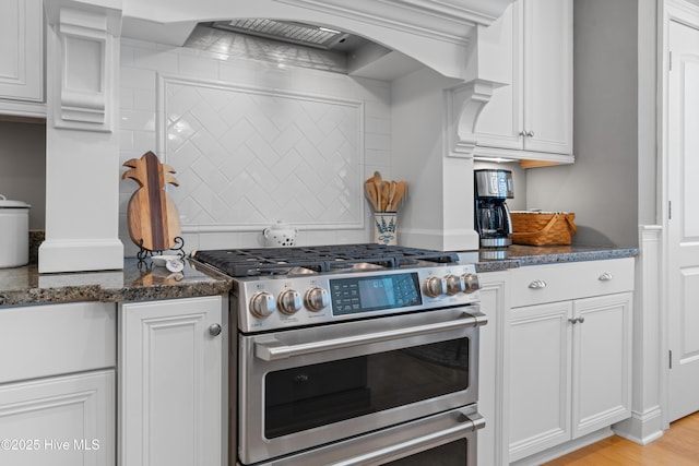 kitchen with white cabinetry, high end range, dark stone counters, and custom range hood