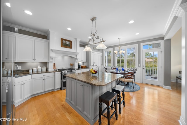 kitchen featuring a kitchen breakfast bar, range with two ovens, white cabinetry, and an island with sink