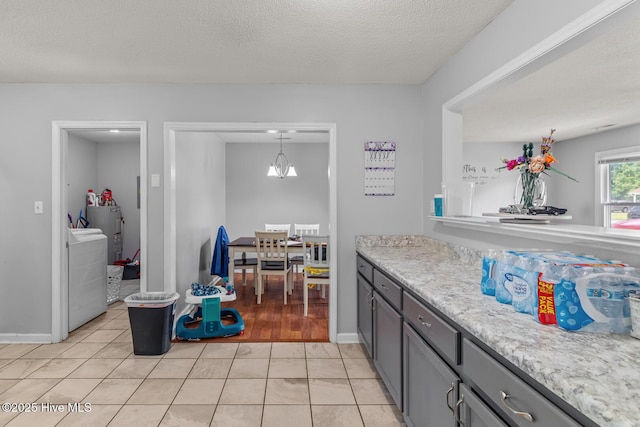 kitchen with an inviting chandelier, hanging light fixtures, light tile patterned floors, a textured ceiling, and washer / clothes dryer