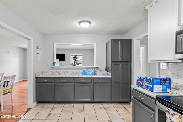 kitchen featuring gray cabinetry, decorative backsplash, light tile patterned floors, a textured ceiling, and light stone counters