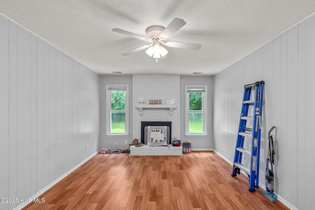 unfurnished living room featuring wooden walls, ceiling fan, light hardwood / wood-style floors, and a brick fireplace