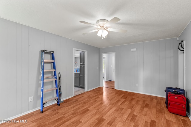 spare room featuring wood walls, ceiling fan, light hardwood / wood-style floors, and a textured ceiling