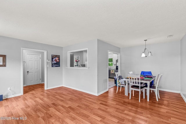 dining space featuring a notable chandelier, light wood-type flooring, and a textured ceiling