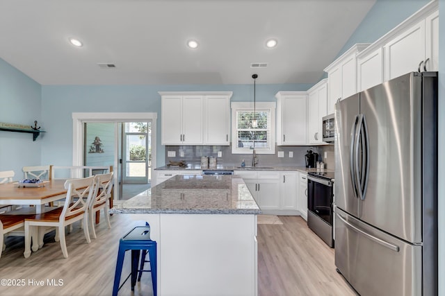 kitchen with light stone countertops, a center island, decorative light fixtures, white cabinets, and appliances with stainless steel finishes