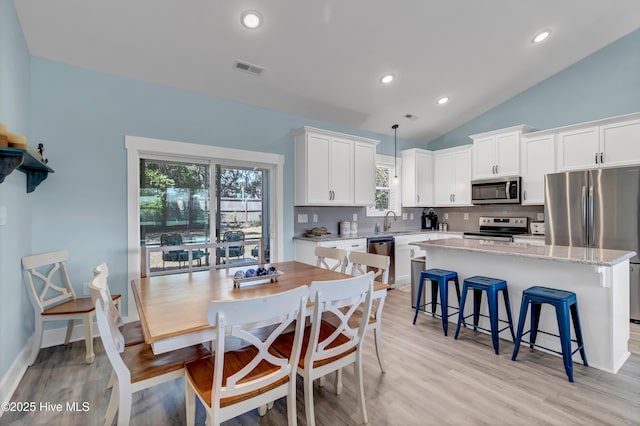 kitchen featuring sink, stainless steel appliances, a kitchen island, decorative light fixtures, and white cabinets