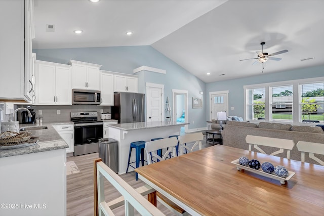 dining space featuring ceiling fan, light wood-type flooring, sink, and high vaulted ceiling