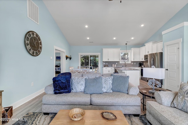 living room featuring light hardwood / wood-style floors, vaulted ceiling, and sink