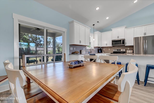 dining area with ceiling fan, sink, light hardwood / wood-style floors, and lofted ceiling