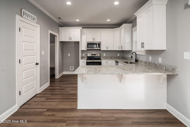 kitchen with appliances with stainless steel finishes, sink, a breakfast bar area, white cabinets, and ornamental molding