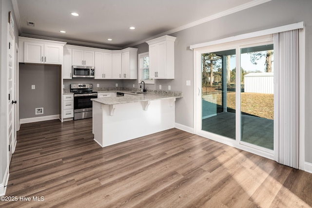 kitchen with appliances with stainless steel finishes, white cabinets, dark hardwood / wood-style flooring, crown molding, and light stone countertops