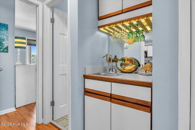 bar with light wood-type flooring, white cabinetry, and sink