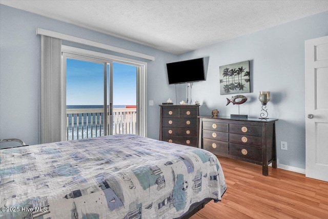 bedroom with access to exterior, a textured ceiling, and light hardwood / wood-style floors