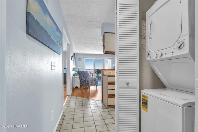 laundry area featuring stacked washer / dryer, light tile patterned flooring, and a textured ceiling