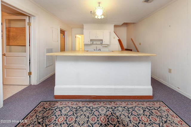 kitchen featuring dark colored carpet, white cabinetry, ornamental molding, and sink