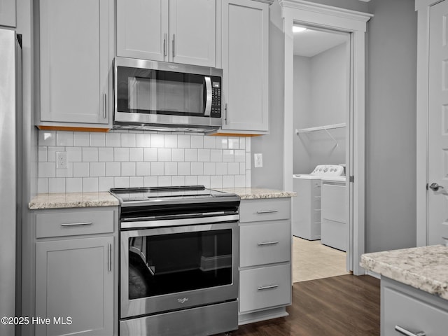 kitchen featuring washer and dryer, light stone counters, stainless steel appliances, and dark wood-type flooring