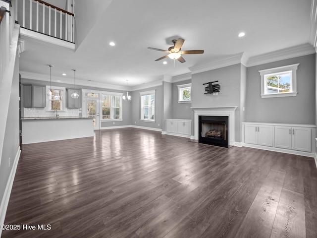 unfurnished living room featuring dark hardwood / wood-style flooring, ceiling fan with notable chandelier, and ornamental molding