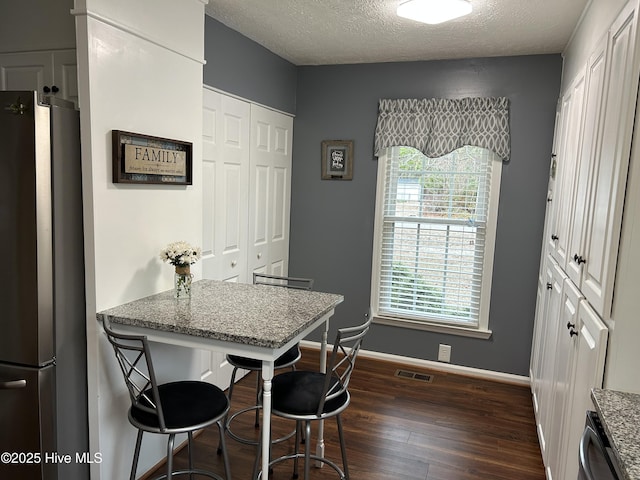 kitchen with a breakfast bar, dark hardwood / wood-style floors, light stone countertops, a textured ceiling, and stainless steel appliances