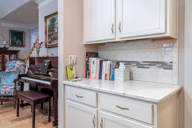 kitchen featuring light stone counters, crown molding, white cabinets, and light wood-type flooring