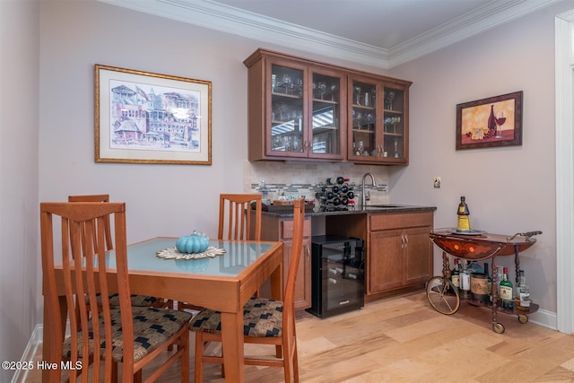 dining room with ornamental molding, light hardwood / wood-style flooring, wine cooler, and indoor wet bar