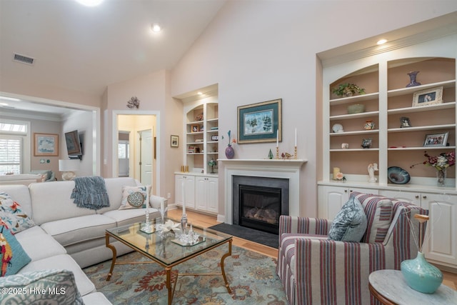 living room with built in shelves, lofted ceiling, and light hardwood / wood-style flooring