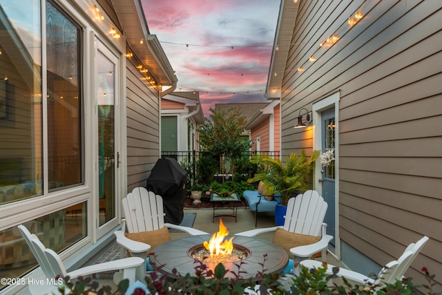 patio terrace at dusk featuring fence, a fire pit, and grilling area