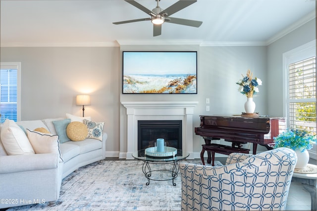 living area featuring ornamental molding, a glass covered fireplace, ceiling fan, and baseboards