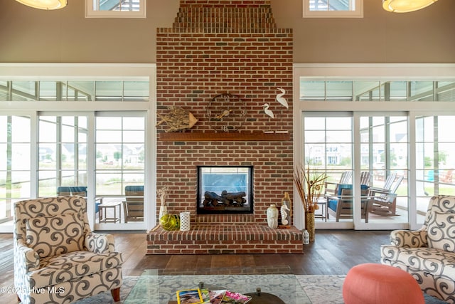 living area featuring a wealth of natural light, a brick fireplace, a towering ceiling, and wood finished floors