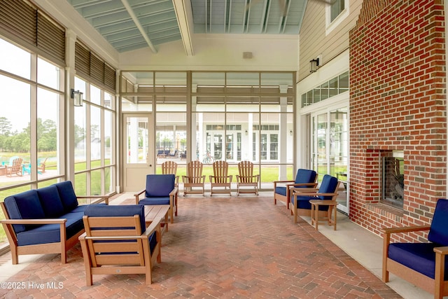 sunroom featuring vaulted ceiling with beams and a brick fireplace