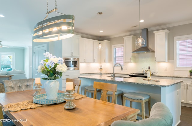 kitchen featuring a center island with sink, stainless steel appliances, crown molding, wall chimney range hood, and a sink