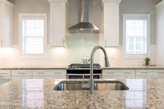 kitchen featuring wall chimney exhaust hood, backsplash, a wealth of natural light, and white cabinetry