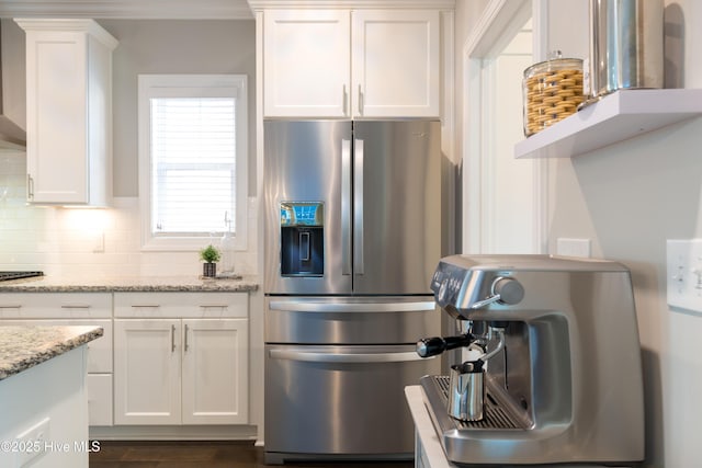 kitchen with light stone counters, decorative backsplash, ornamental molding, white cabinetry, and stainless steel fridge