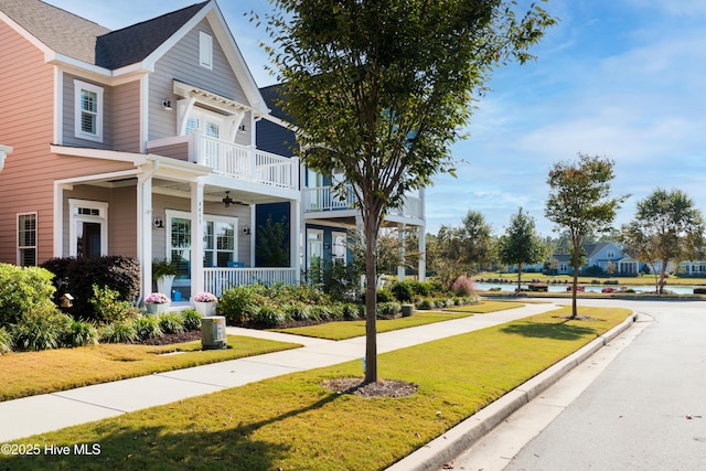 exterior space featuring covered porch, a front lawn, a balcony, and a ceiling fan