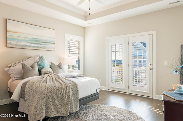 bedroom featuring access to outside, a raised ceiling, multiple windows, and wood finished floors