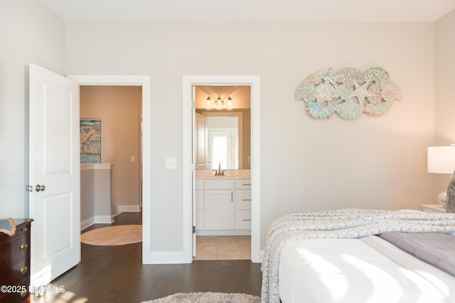 bedroom featuring connected bathroom, dark wood-style flooring, a sink, and baseboards