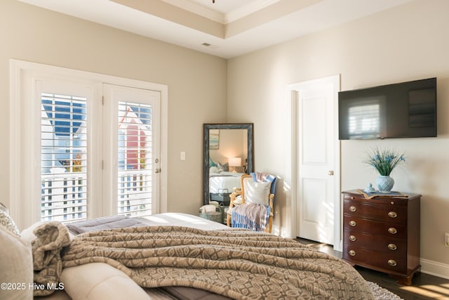 bedroom with access to exterior, a tray ceiling, ornamental molding, wood finished floors, and baseboards