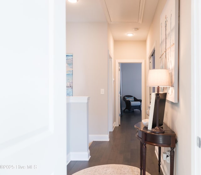 hallway featuring dark wood-type flooring, attic access, and baseboards