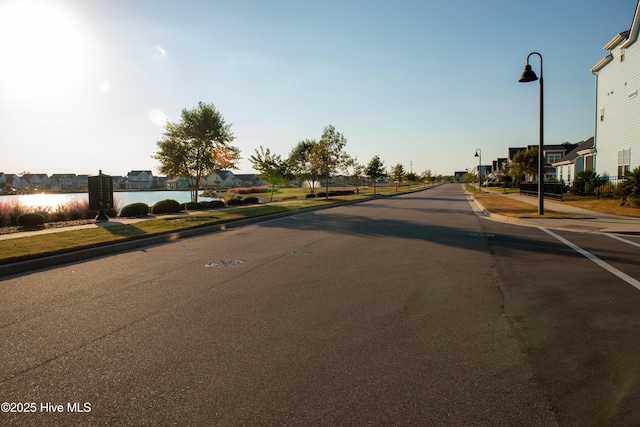 view of road featuring street lighting, a residential view, curbs, a water view, and sidewalks