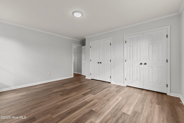 unfurnished bedroom with hardwood / wood-style floors, crown molding, and two closets