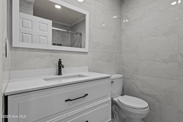 bathroom with vanity, crown molding, tile walls, toilet, and a shower with shower door