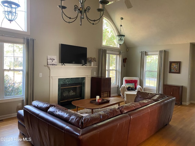 living room featuring a premium fireplace, light hardwood / wood-style floors, vaulted ceiling, and a notable chandelier