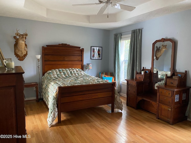 bedroom featuring a tray ceiling, ceiling fan, and light wood-type flooring