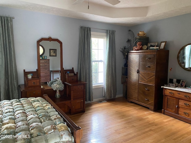 bedroom featuring a tray ceiling, ceiling fan, light hardwood / wood-style flooring, and a textured ceiling