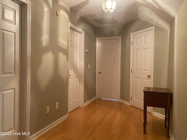 hallway with lofted ceiling, light wood-type flooring, and a textured ceiling