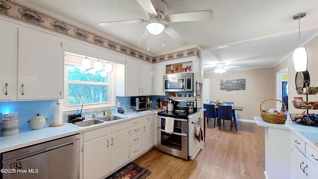 kitchen with appliances with stainless steel finishes, sink, pendant lighting, white cabinets, and light hardwood / wood-style floors