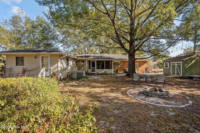 back of property featuring a fire pit, a storage unit, and central air condition unit