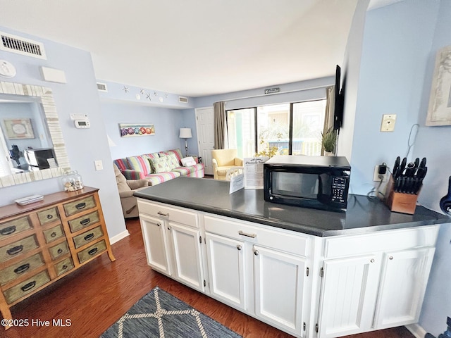 kitchen featuring dark countertops, black microwave, white cabinets, and visible vents