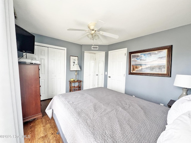 bedroom featuring light wood-type flooring, a ceiling fan, visible vents, and multiple closets